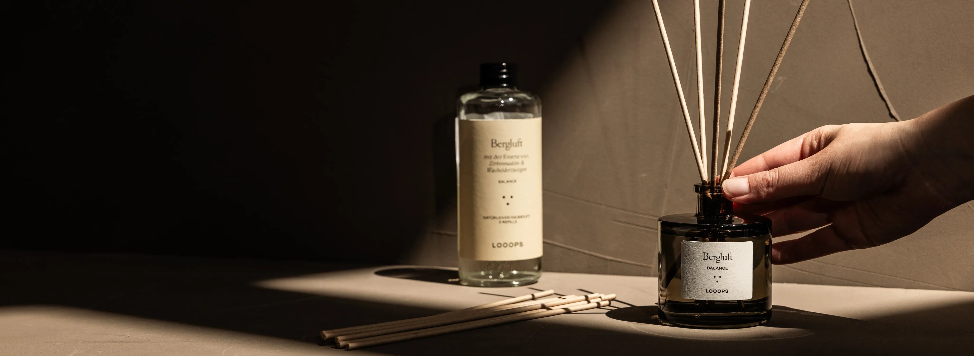 Hand reaches for Reed diffuser, glass bottle in the background