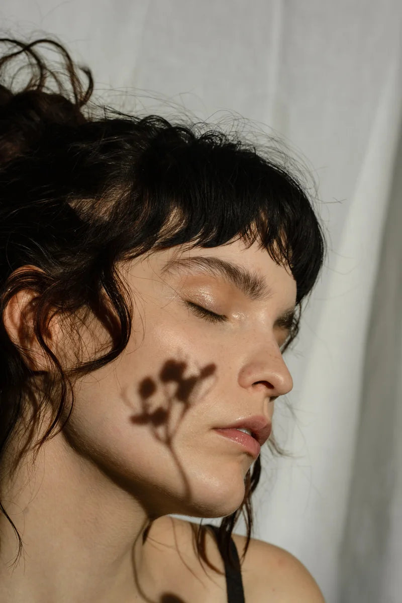 A lady relaxes and has the shadow of a flower on her face.