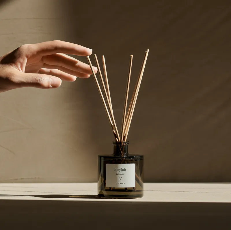 Ein Stäbchen Diffuser wird von einer Hand berührt. 