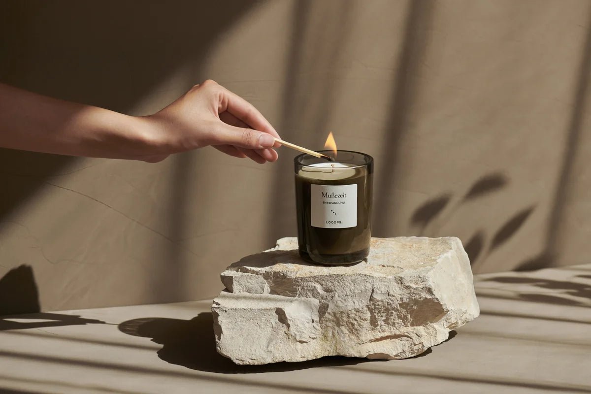 A burning scented candle stands on a stone.