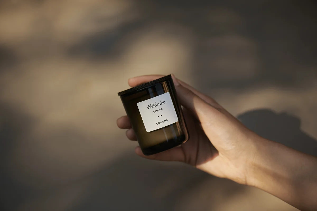 A small scented candle is held in the hand.