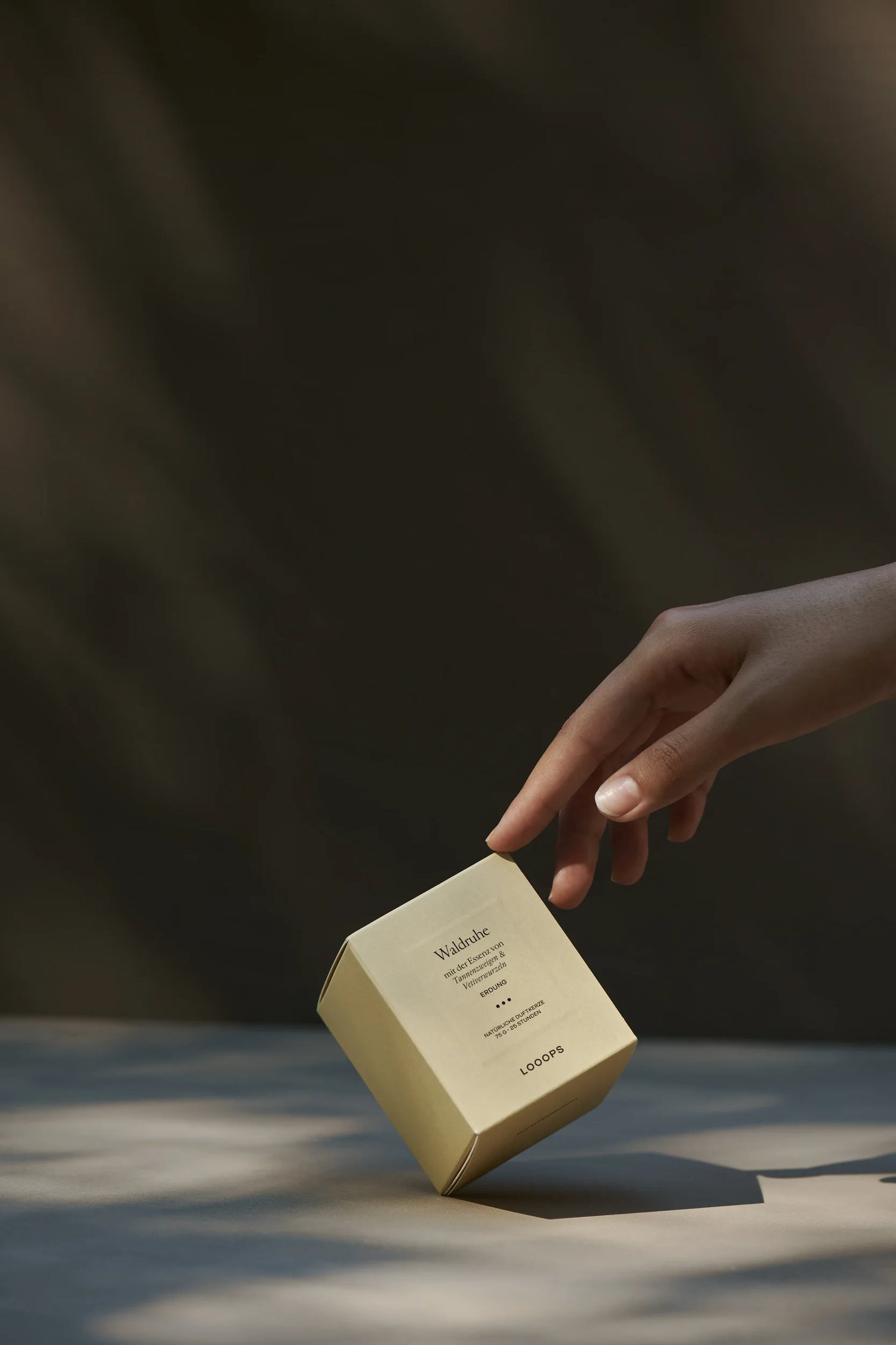 Packaging of a small Waldruhe candle that is poked by a hand